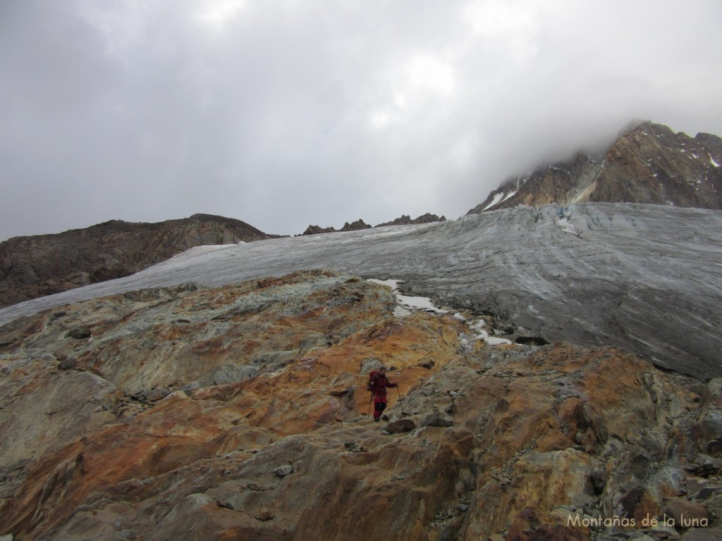 Joaquín dejando el primer glaciar y bajando por el espolón rocoso en busca del refugio, arriba el pico cubierto